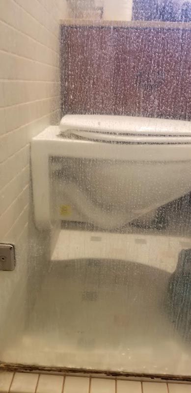 A toilet is sitting in a bathroom behind a glass door.