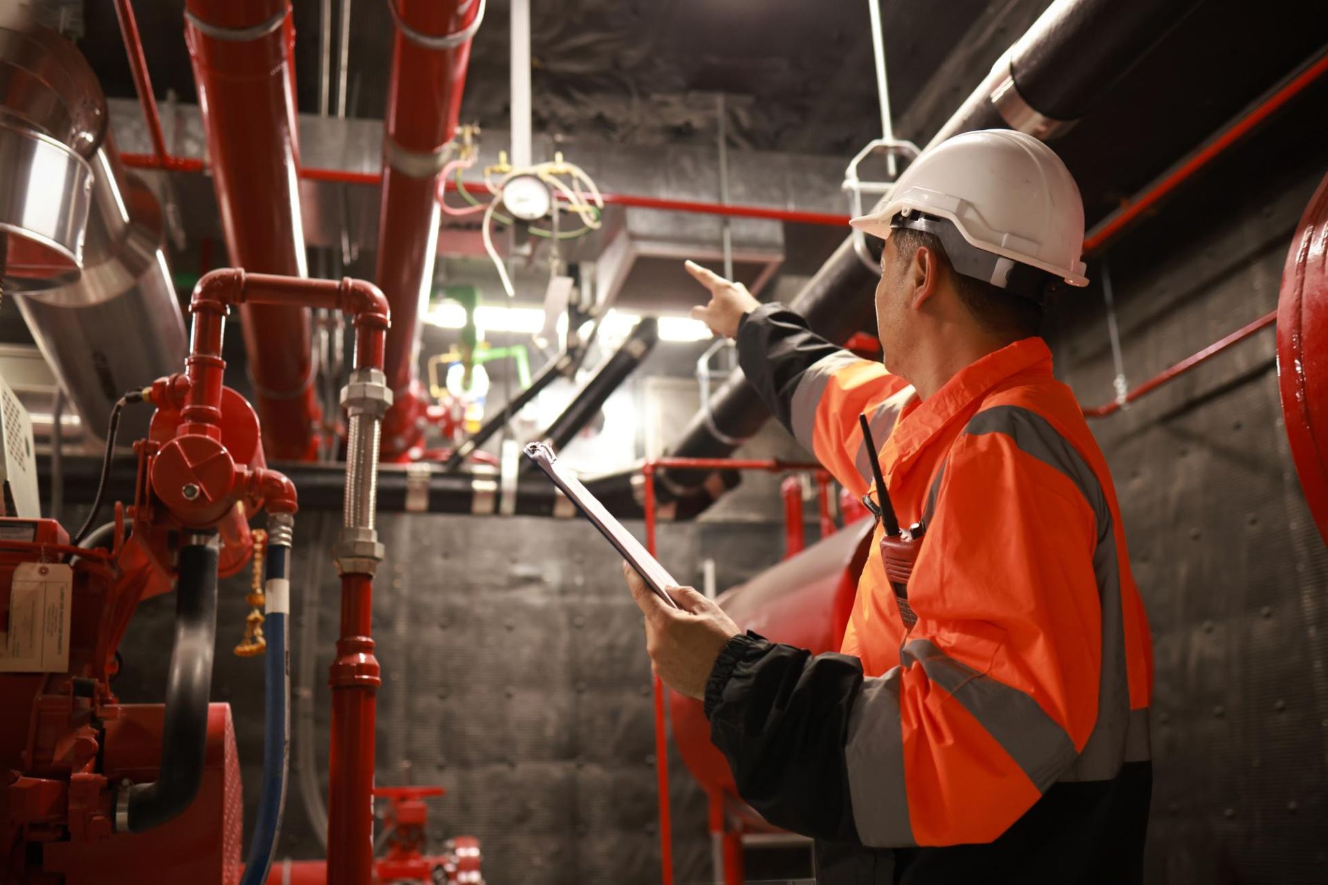 A man is standing in a room with pipes and looking at a tablet.