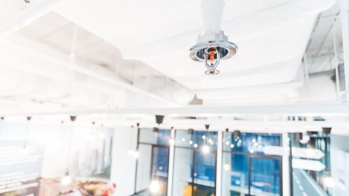 A fire sprinkler is hanging from the ceiling of an office building.