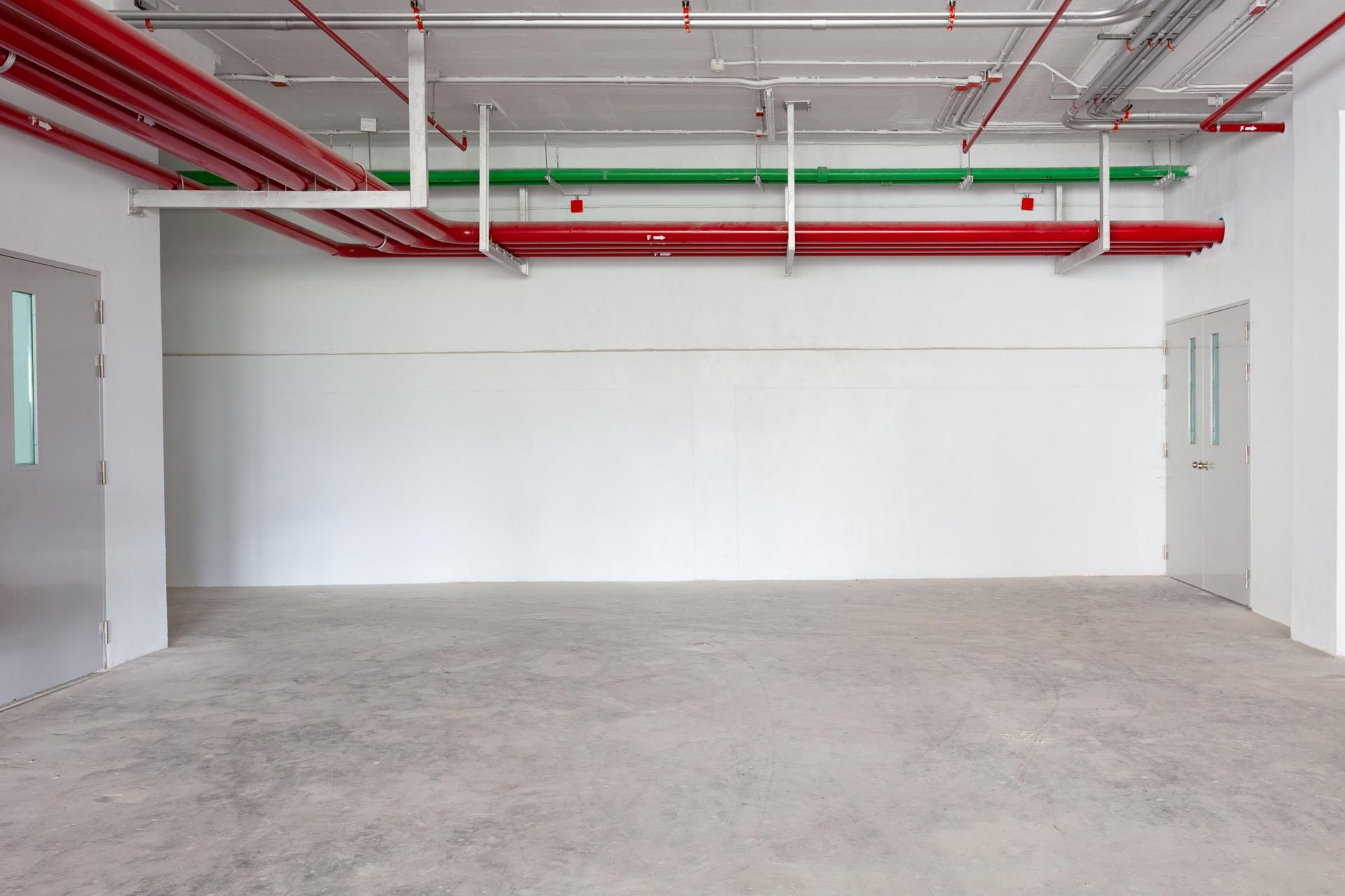 An empty room with red and green pipes hanging from the ceiling.