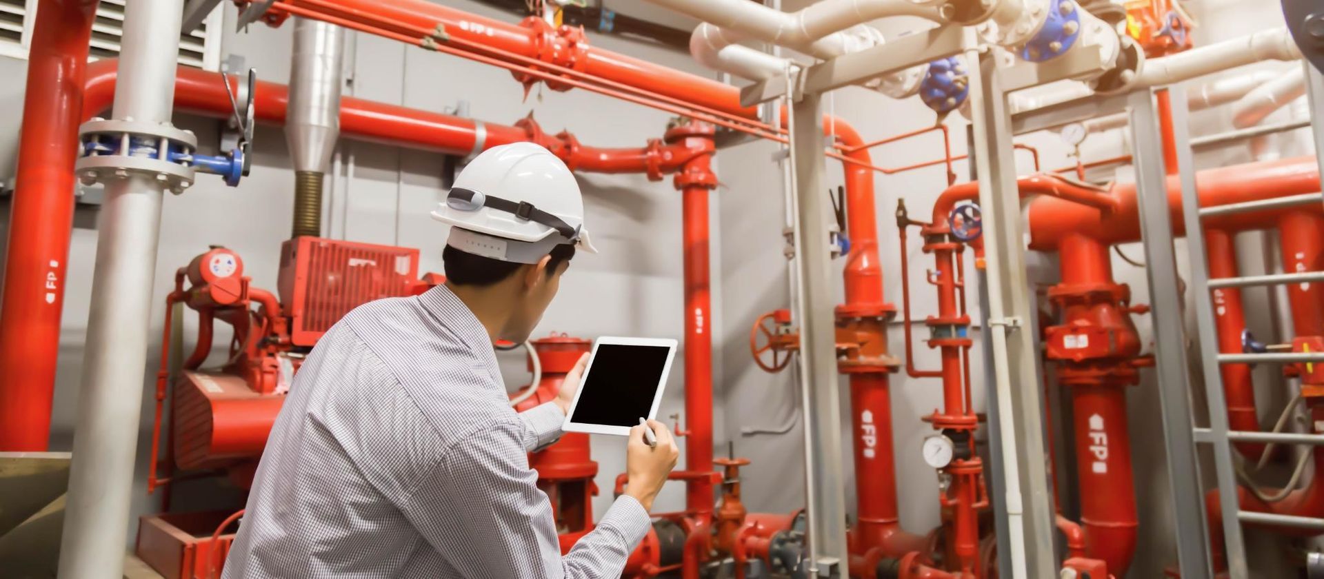 A man is using a tablet in a room filled with red pipes.
