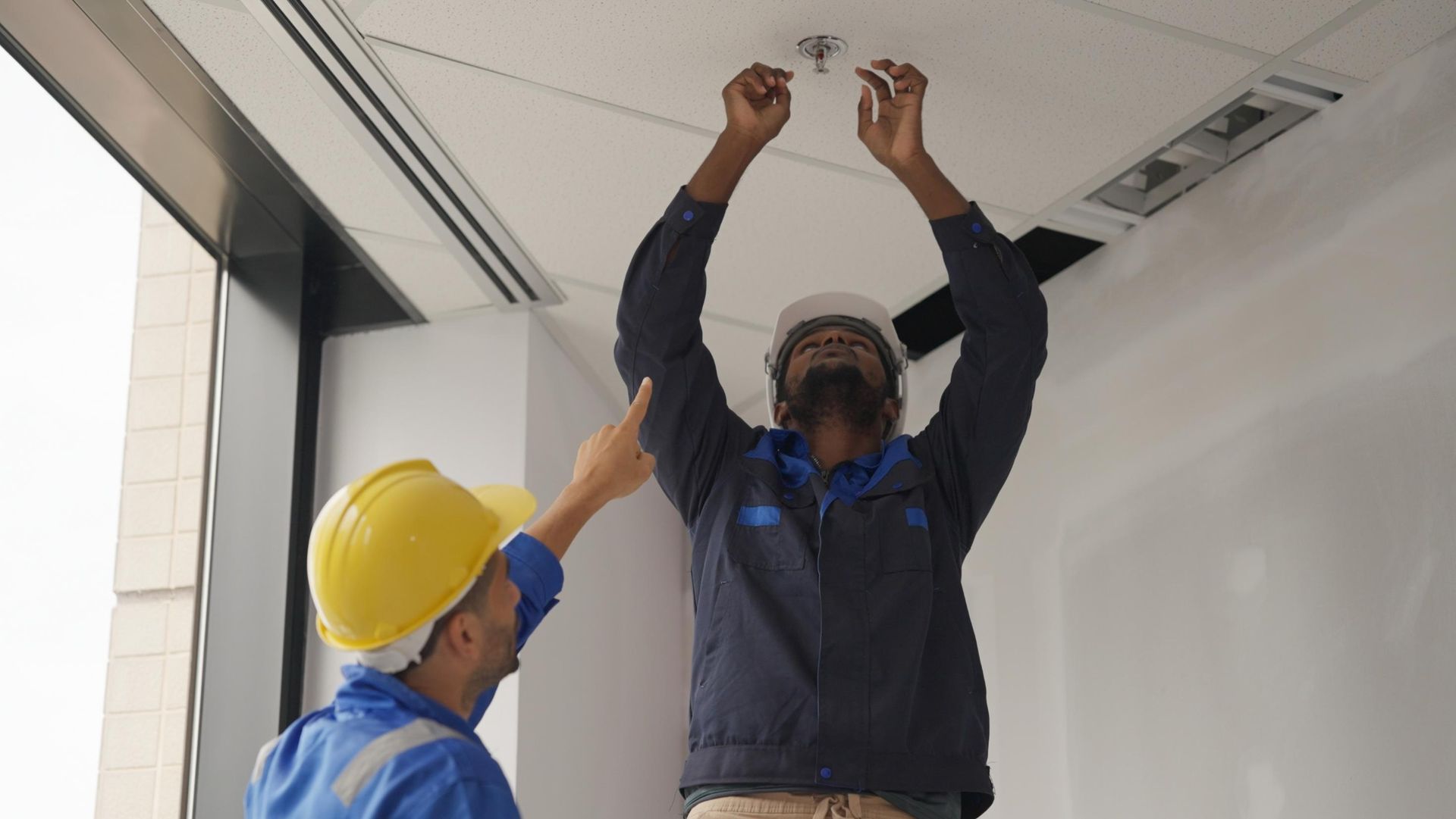 Two men in hard hats are working on a ceiling.