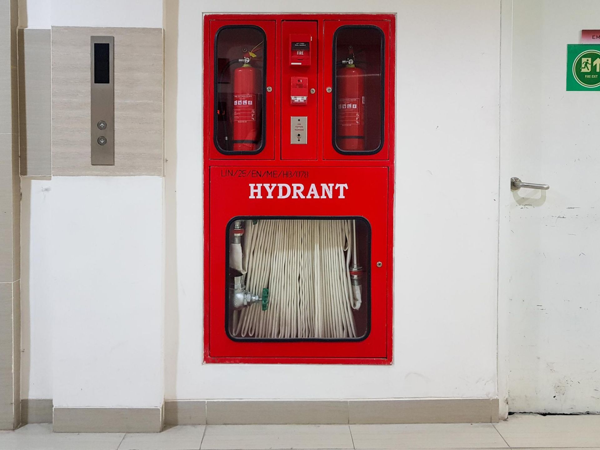 A red fire hydrant is hanging on a white wall.