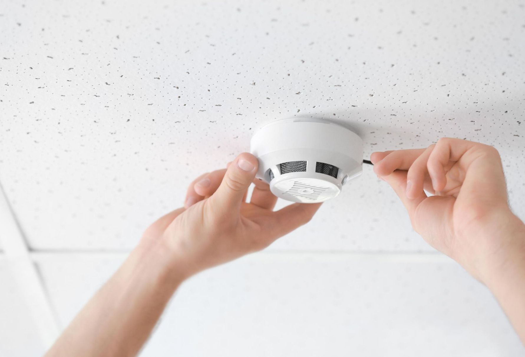 A person is installing a smoke detector on the ceiling.