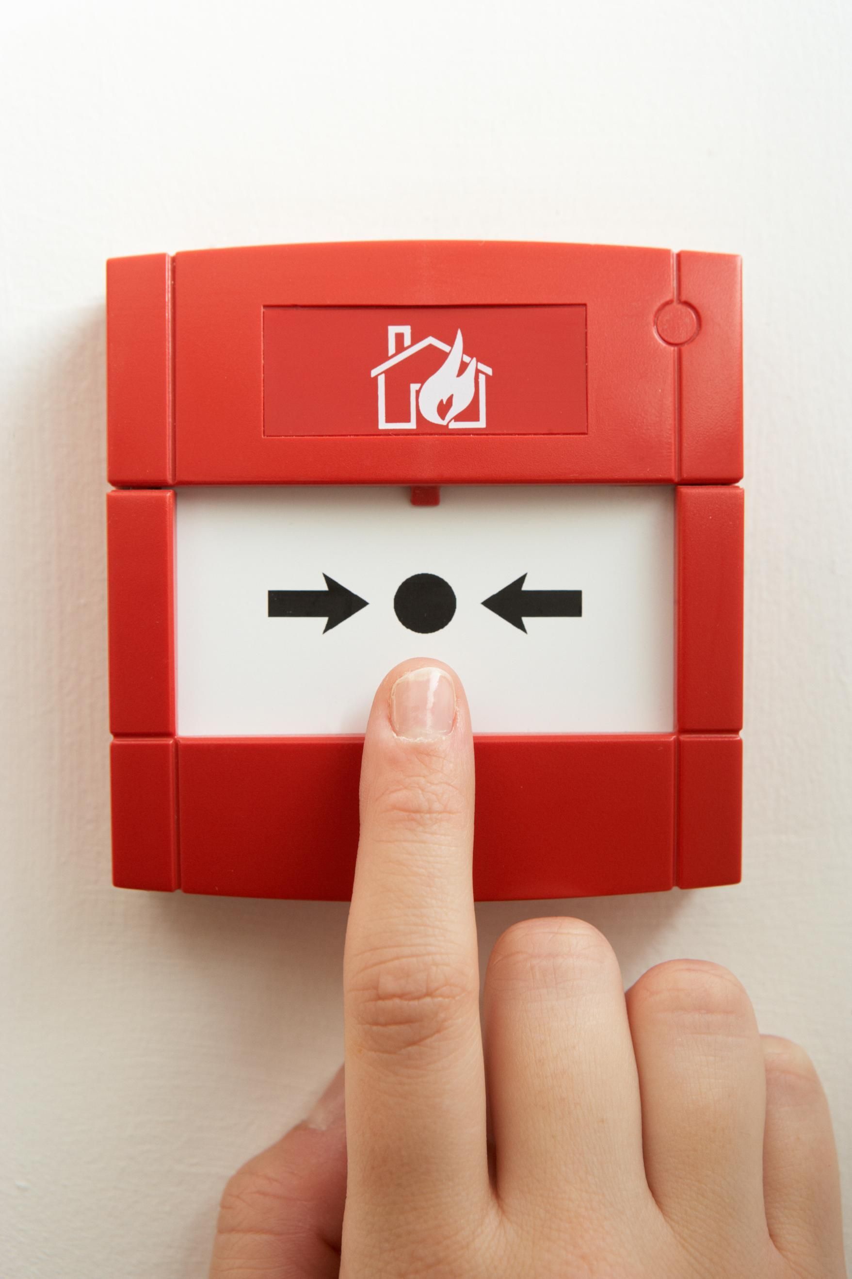 A person is pressing a red fire alarm button with their finger.
