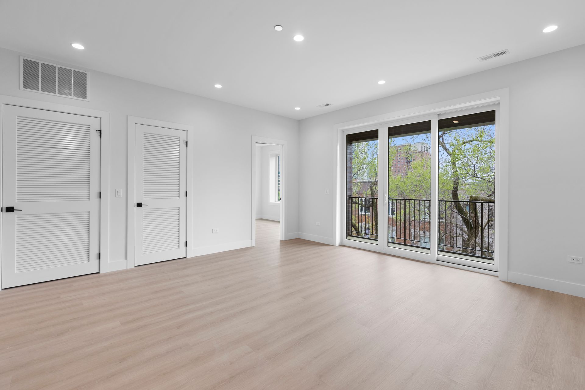 An empty living room with hardwood floors and sliding glass doors.