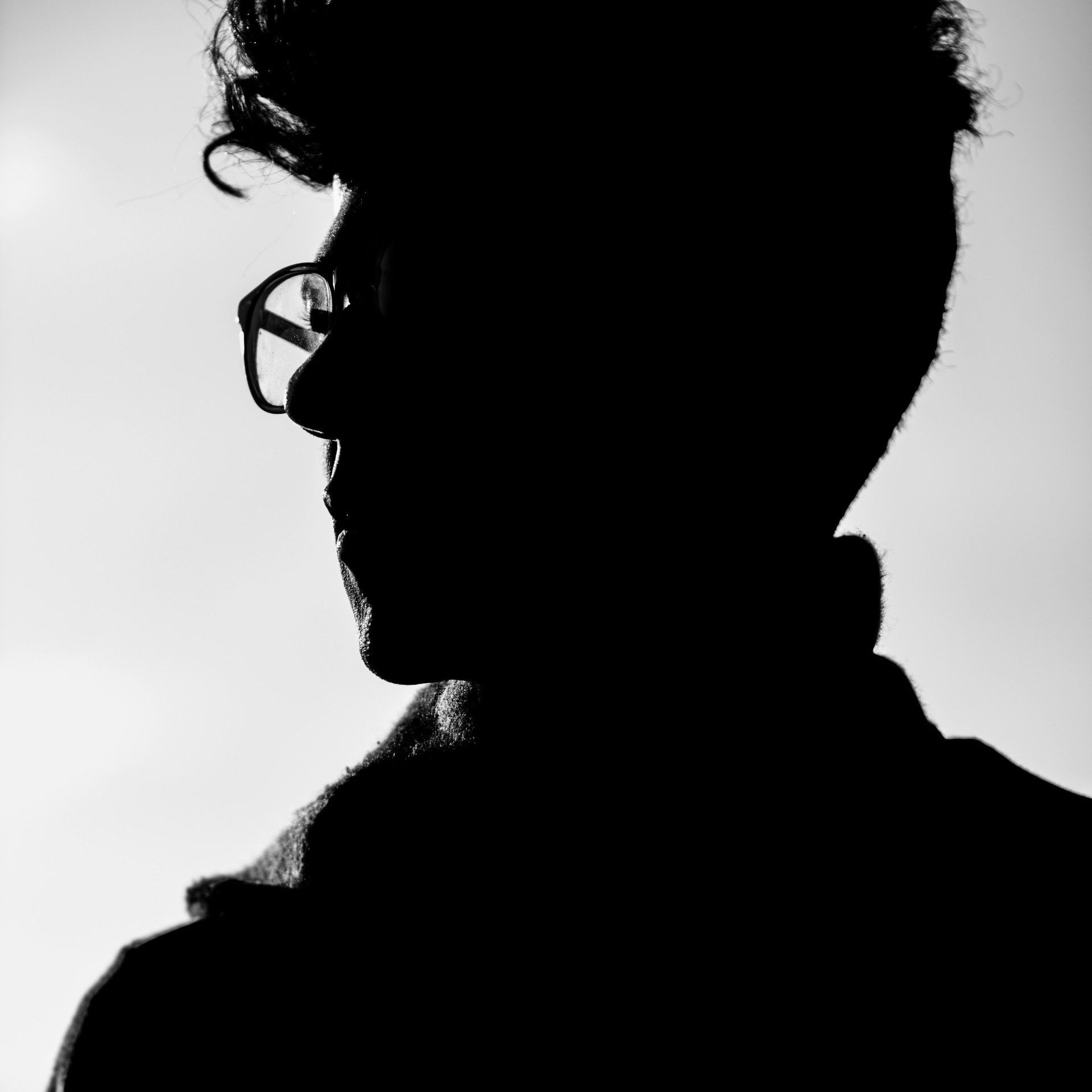 A black and white silhouette of a man wearing glasses.