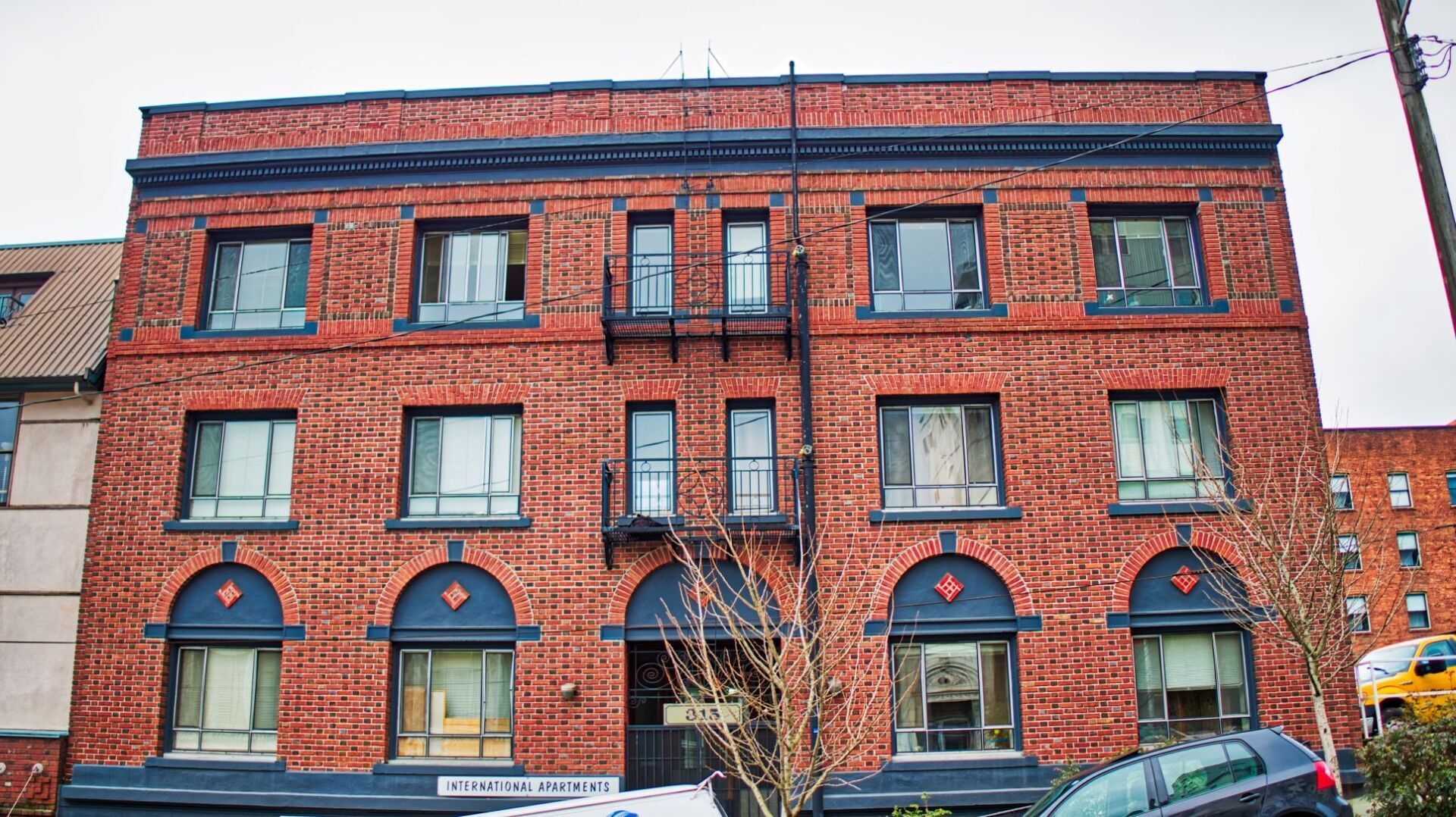 A large red brick building with a fire escape and cars parked in front of it.