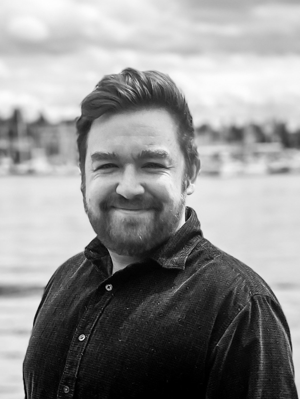 A man with a beard is smiling in a black and white photo.