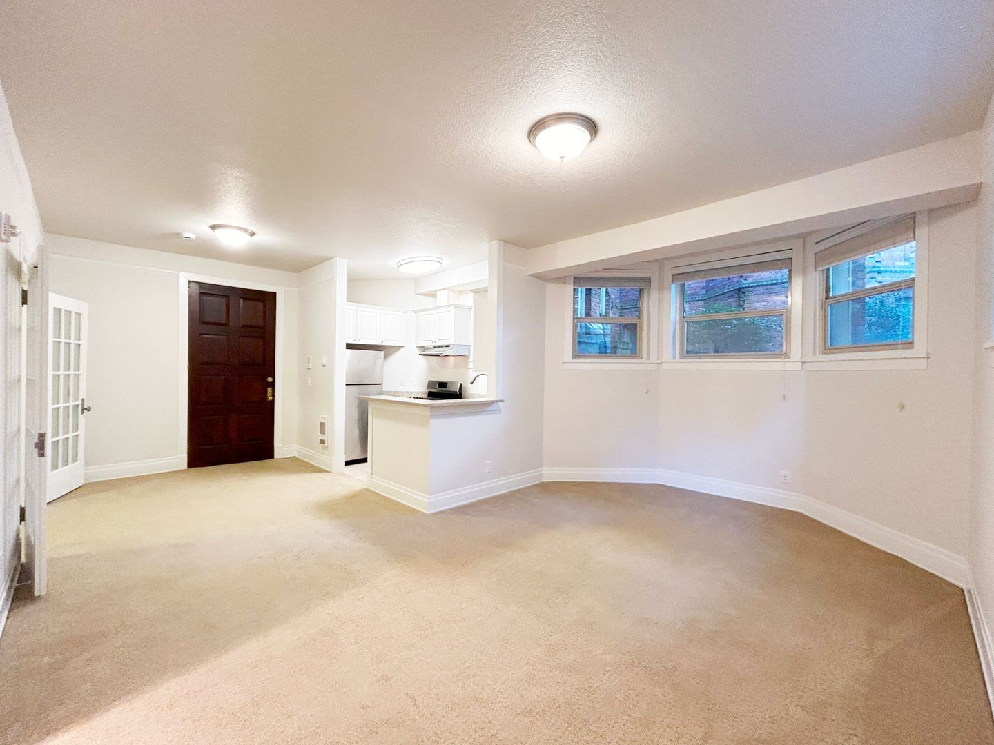 An empty living room with a curved carpet and a kitchen in the background.