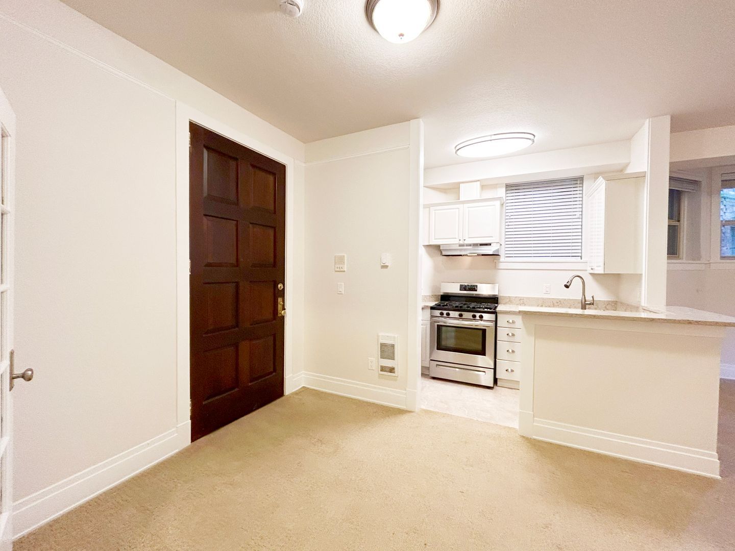 An empty room with a stove and a door leading to a kitchen.