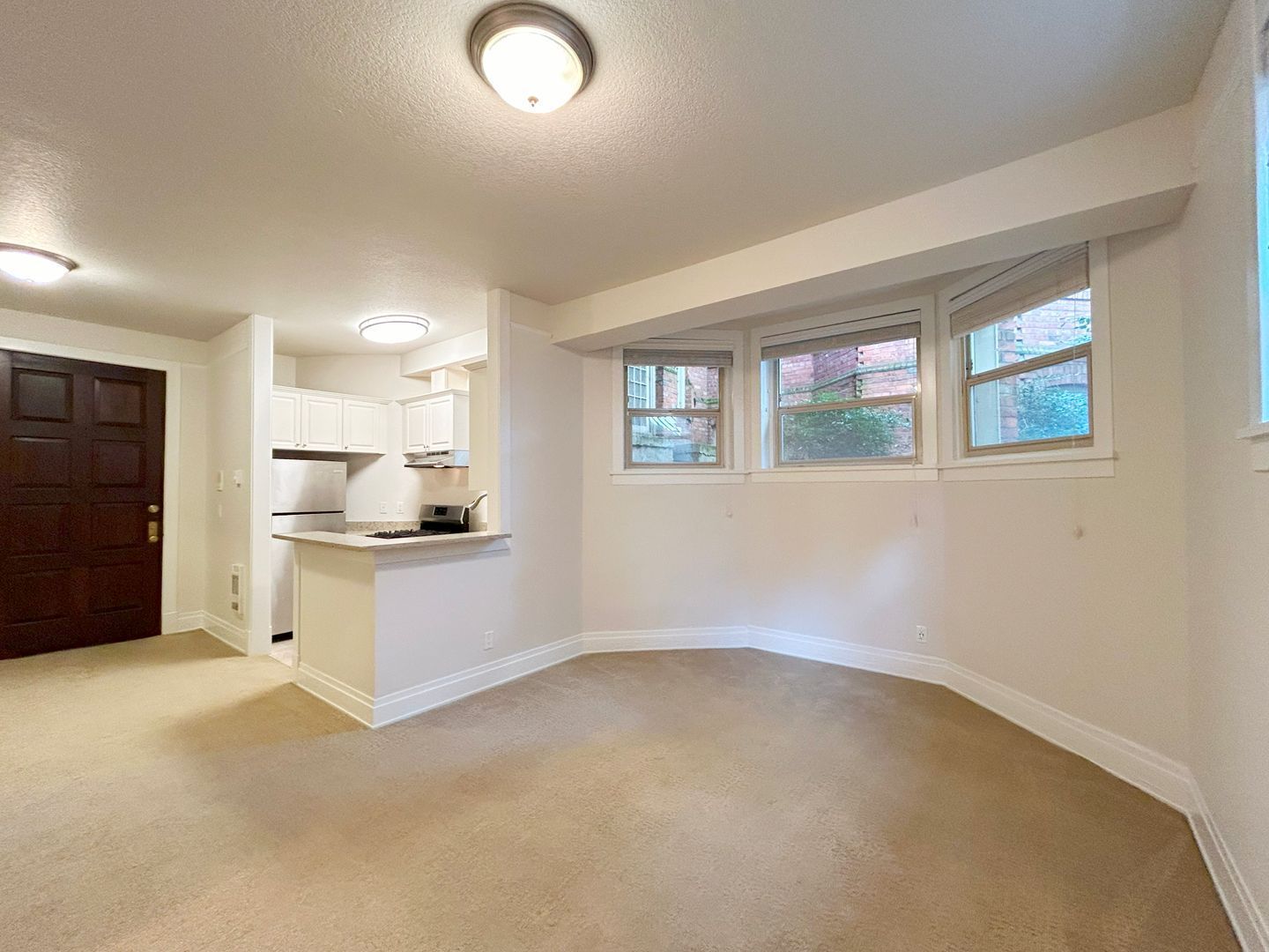 An empty living room with a kitchen in the background.