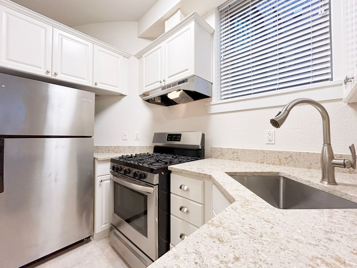 A kitchen with a stove , refrigerator , sink and window.