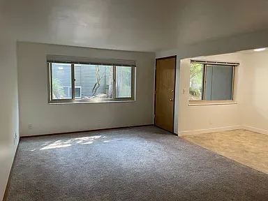 An empty living room with hardwood floors and a large window.