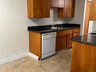 An empty living room with a kitchen in the background.