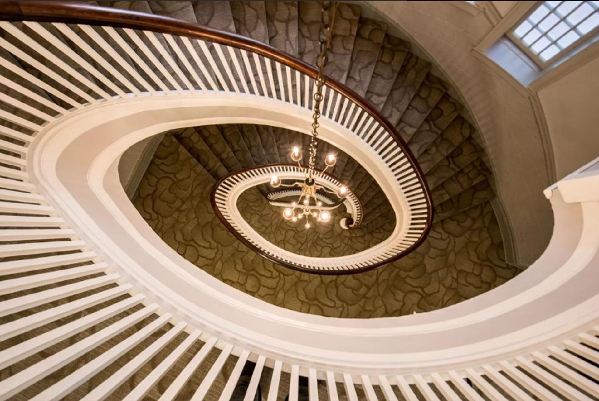 Looking up at a spiral staircase with a chandelier hanging from the ceiling