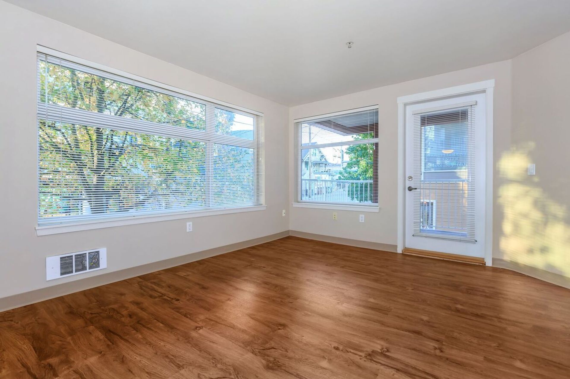 An empty living room with hardwood floors and large windows.