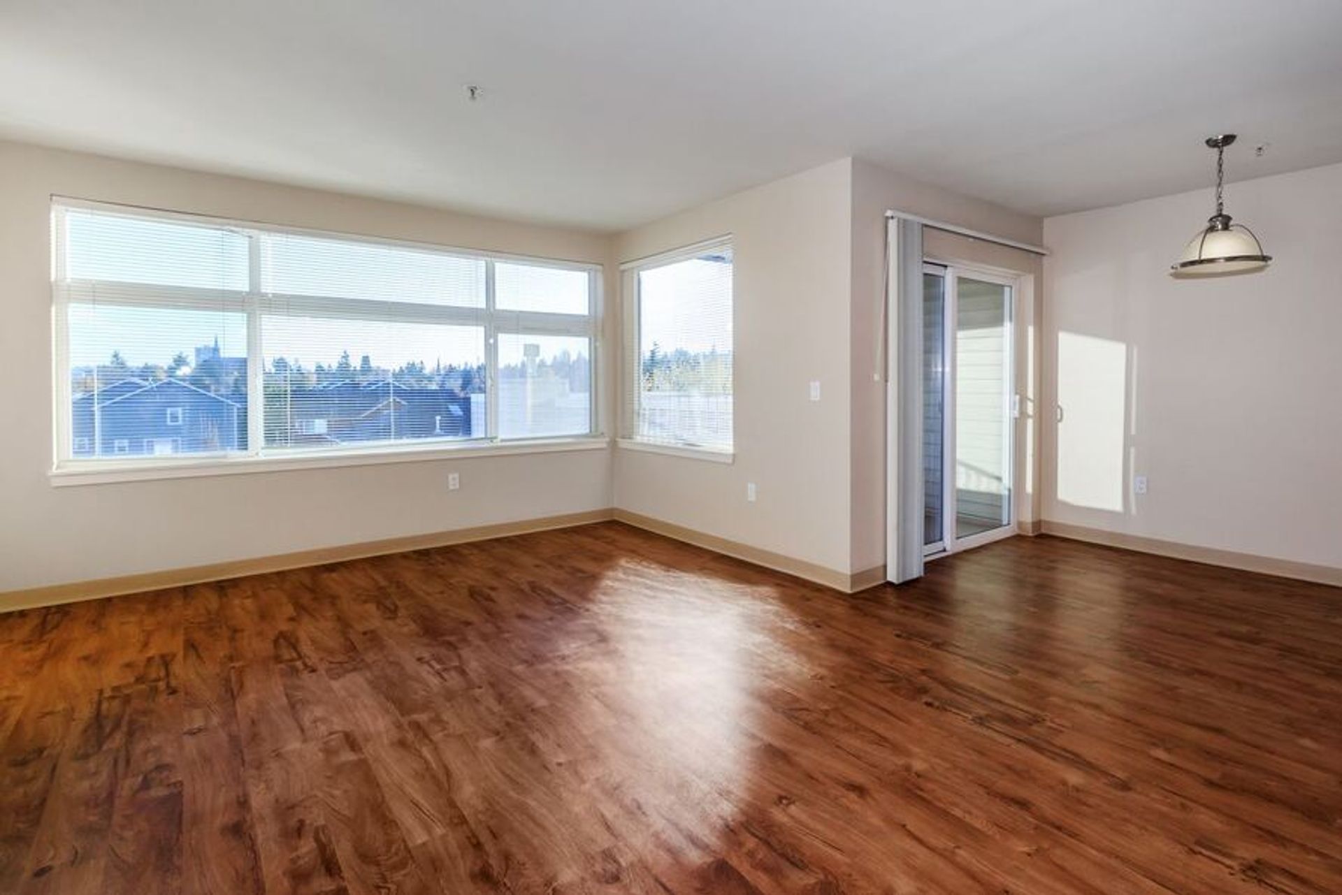 An empty living room with hardwood floors and a sliding glass door.