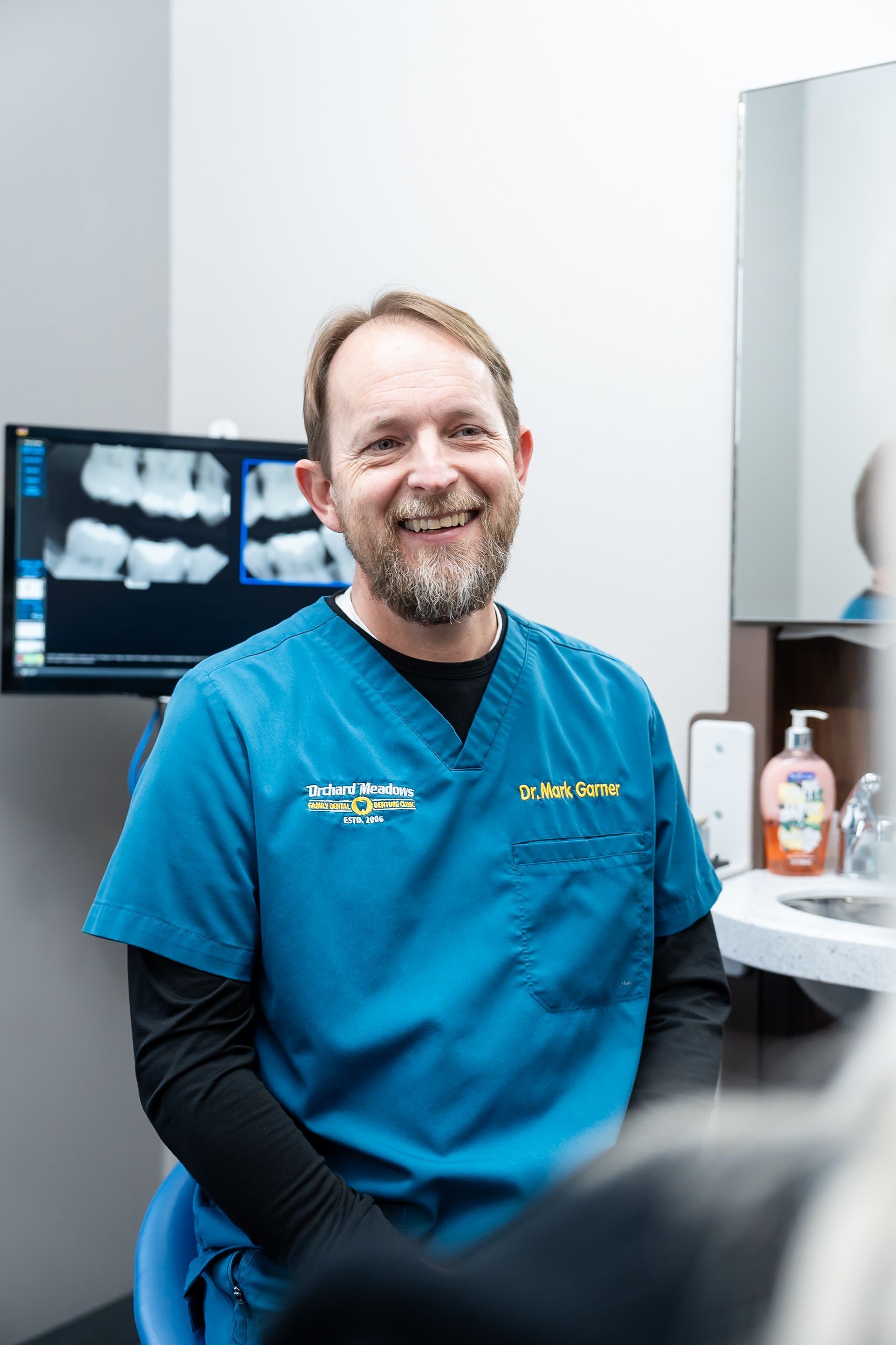 Dr. Garner sitting in a clinical exam room with dental X-rays displayed on a monitor.
