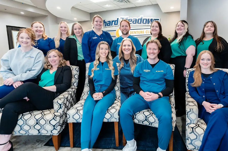 Orchard Meadows dental staff in scrubs and professional attire posing for a photo in a modern office lobby.