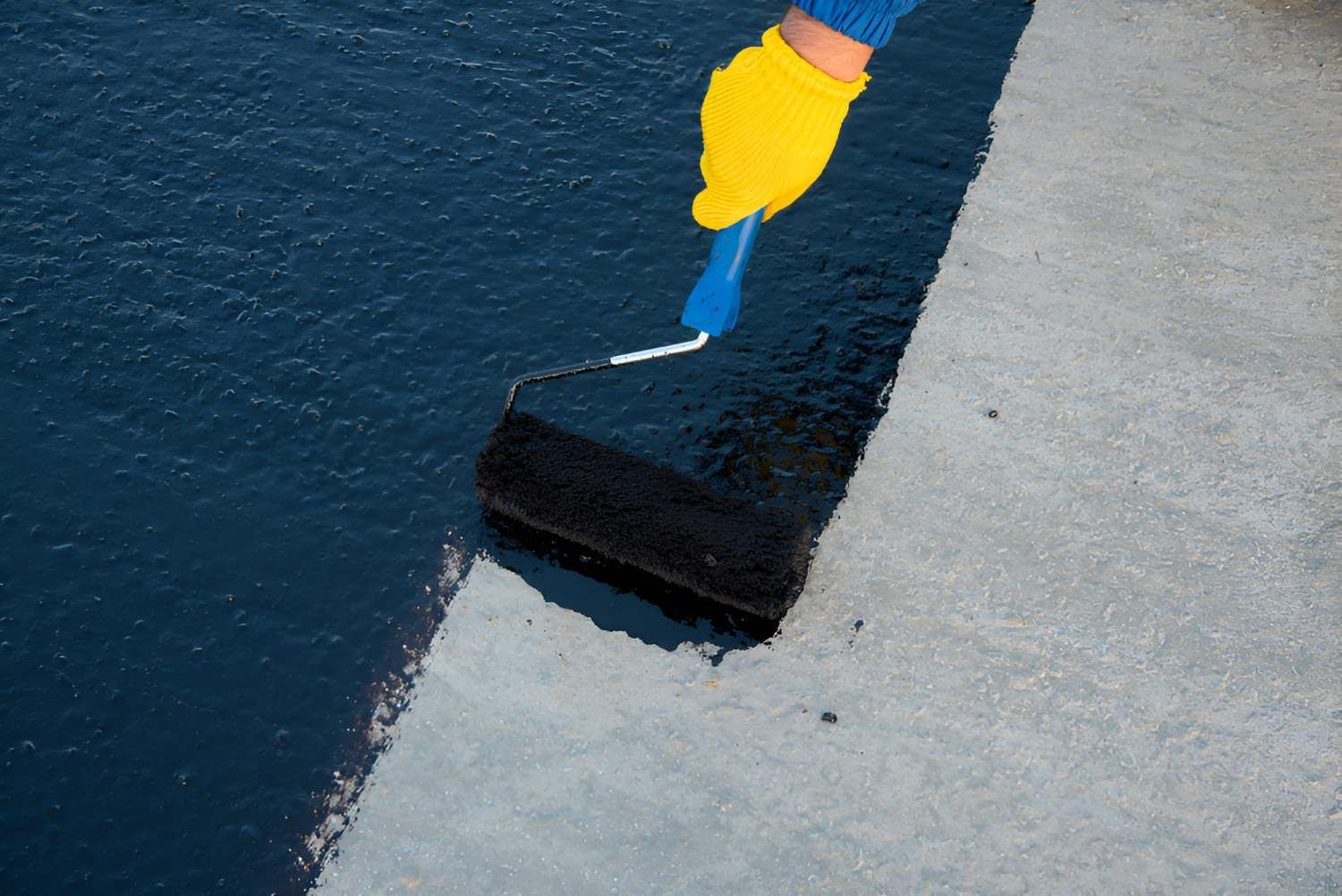 A Person Is Painting A Concrete Surface With A Roller Using Liquid Waterproofing — Bananacoast Waterproofing in Korora, NSW