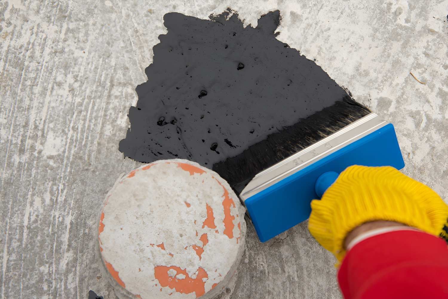 Roofer's hand in yellow mittens holding a brush with Liquid Waterproofing — Bananacoast Waterproofing in Korora, NSW