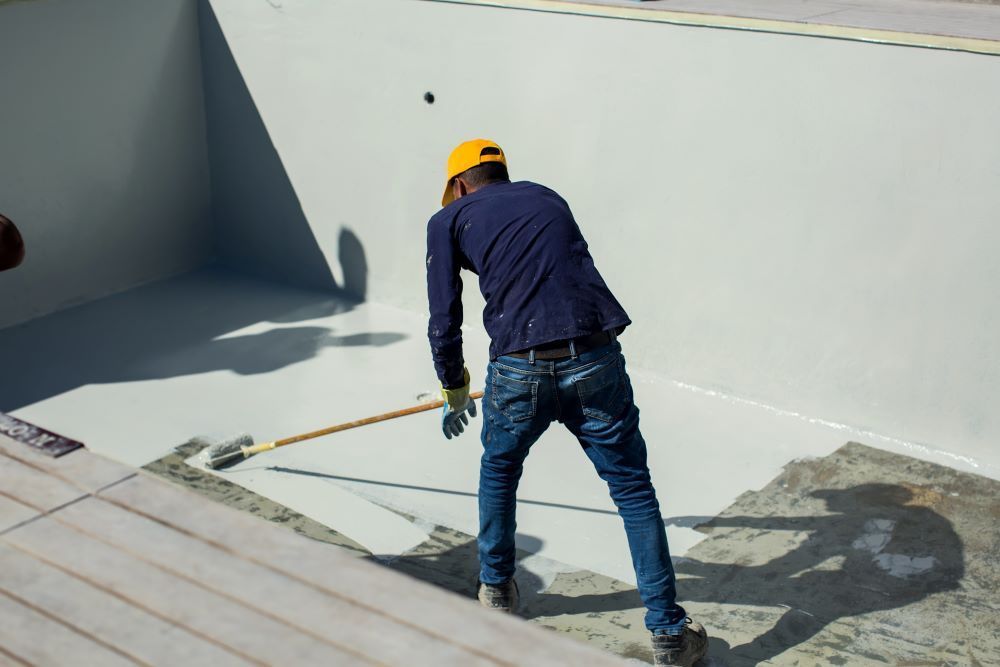 A Man Is Using A Broom To Coat The Pool With Liquid Waterproofing — Bananacoast Waterproofing in Korora, NSW