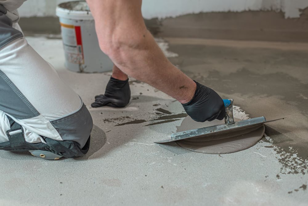 A Man Is Spreading Concrete On The Waterproofing Floor — Bananacoast Waterproofing in Nambucca Heads, NSW