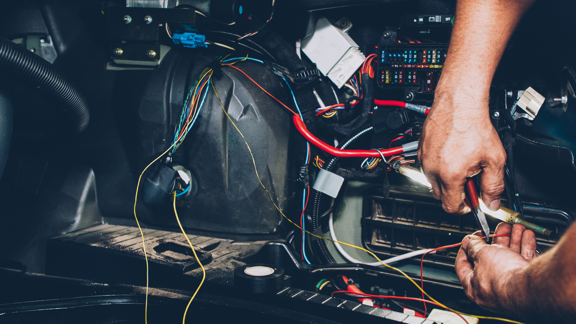 A man is working on a car with a pair of pliers.