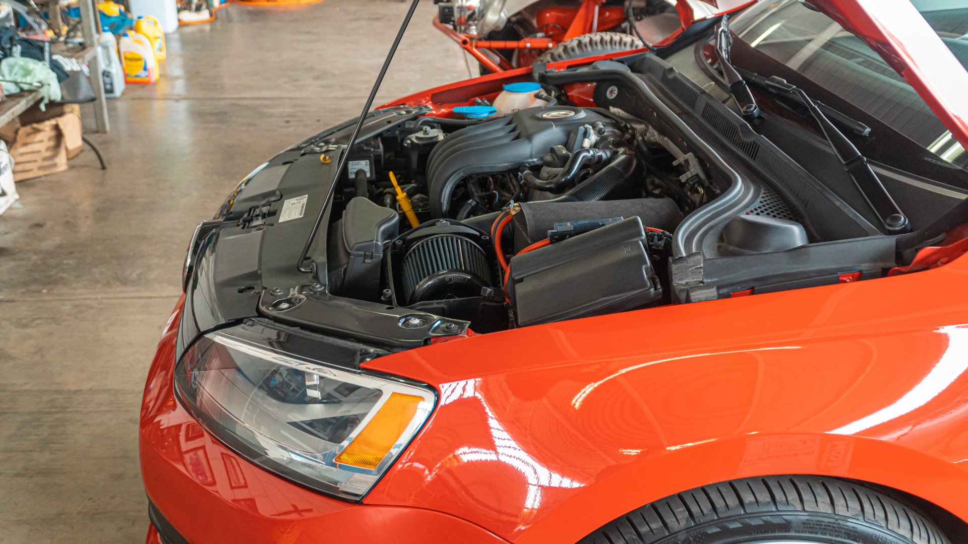 A red car with its hood open in a garage.