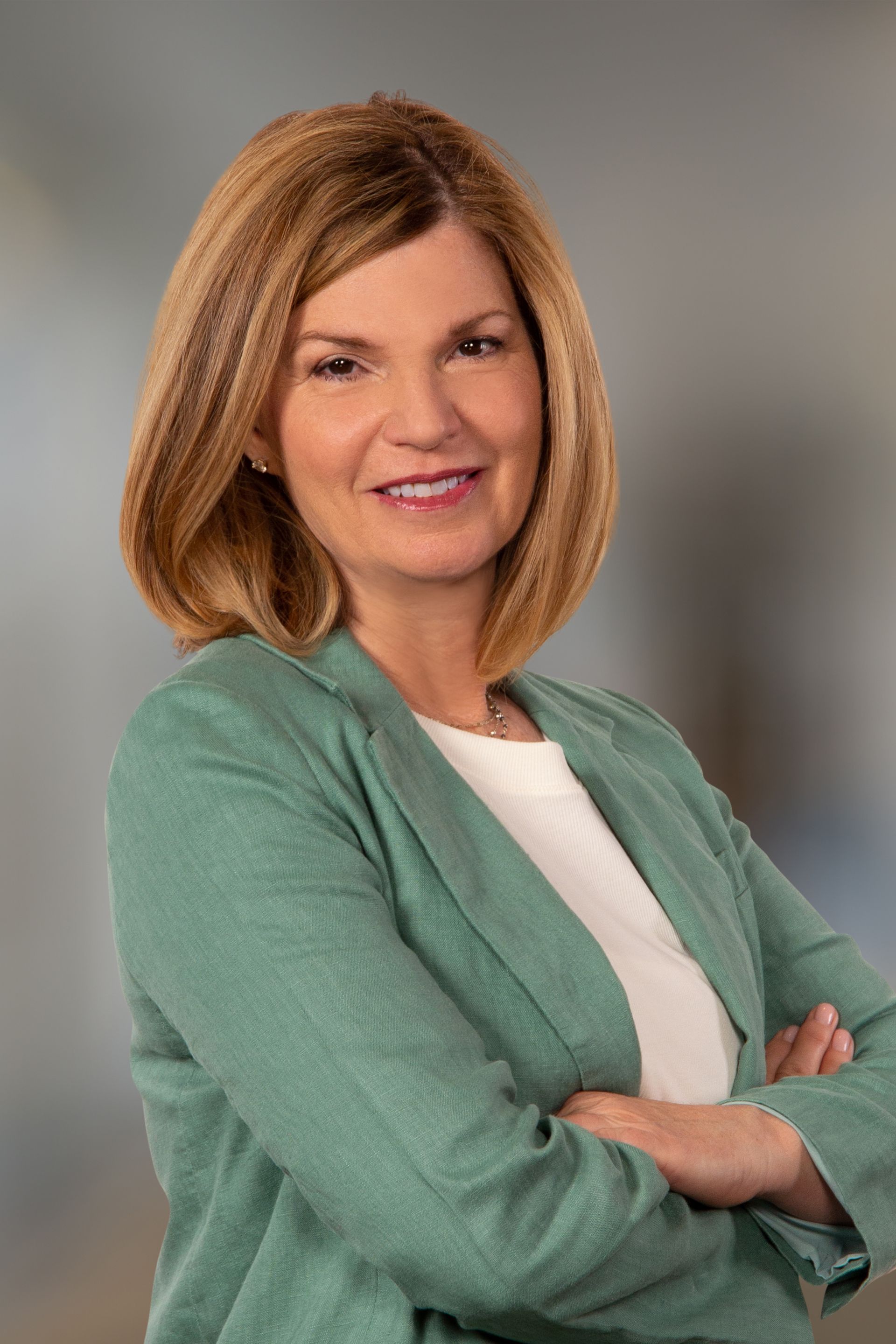 Woman with short blonde hair wearing a green blazer and white shirt, arms crossed, smiling in a professional setting.