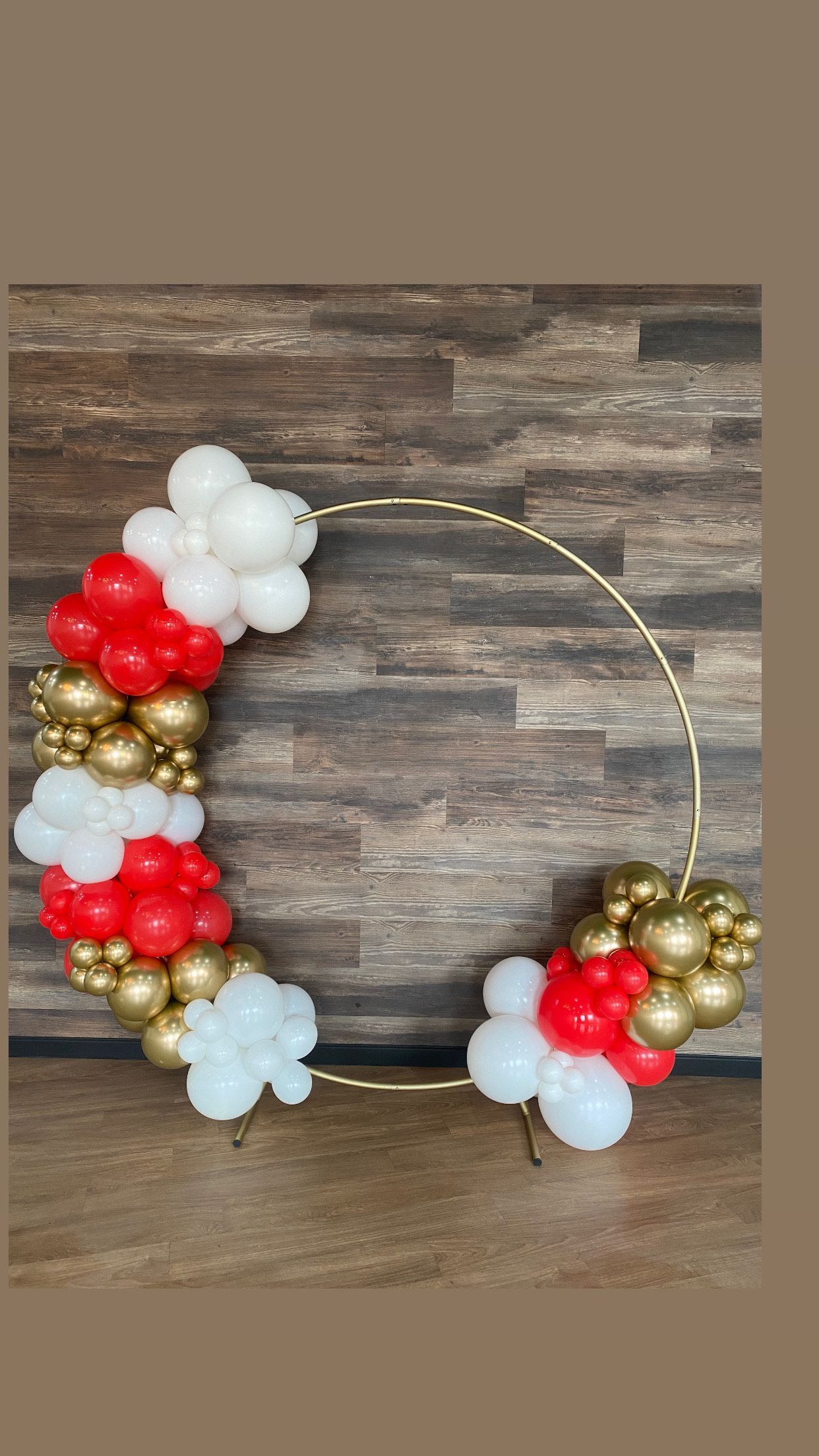 A wreath made of red , white and gold balloons is sitting on a wooden table.