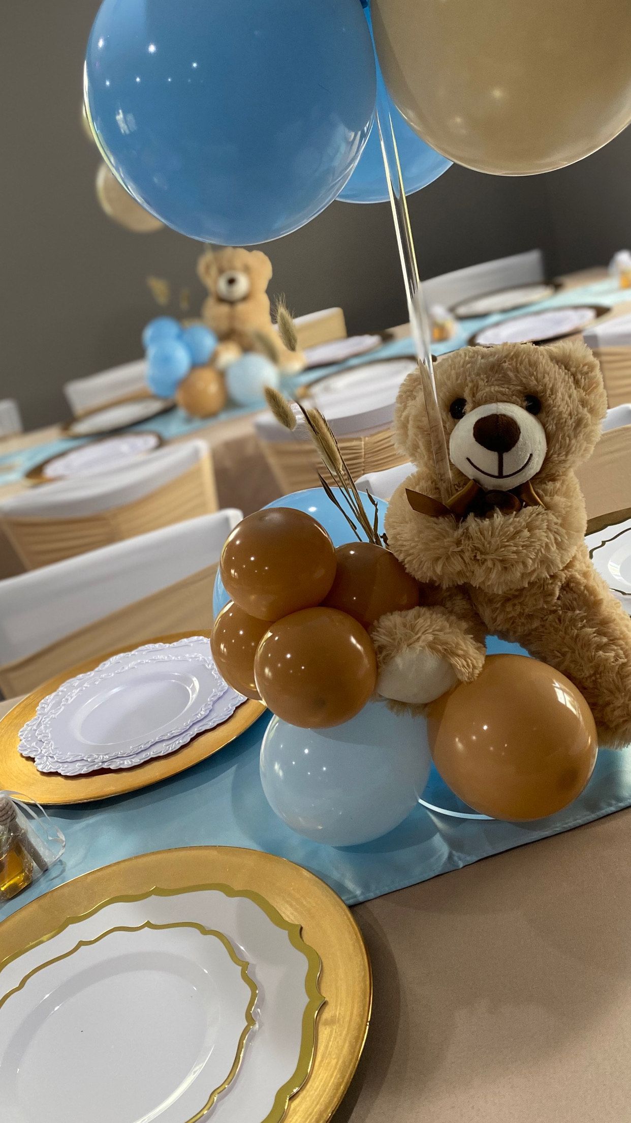 A teddy bear is sitting on top of a table with balloons.