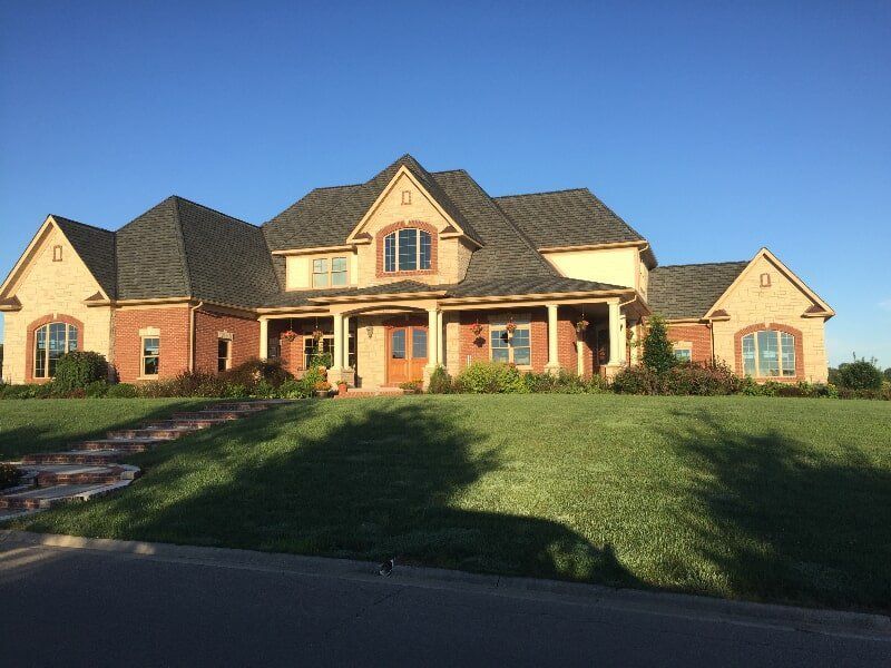 A large brick house with a gray roof is sitting on top of a lush green hillside.