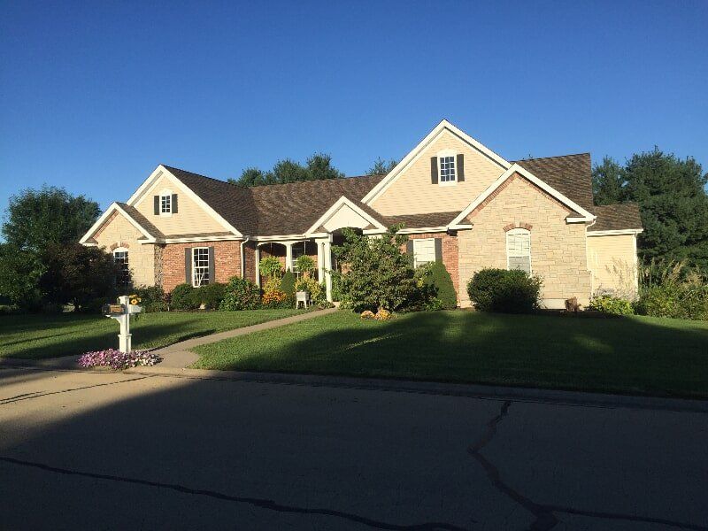 A large brick house with a brown roof is sitting on top of a lush green lawn.