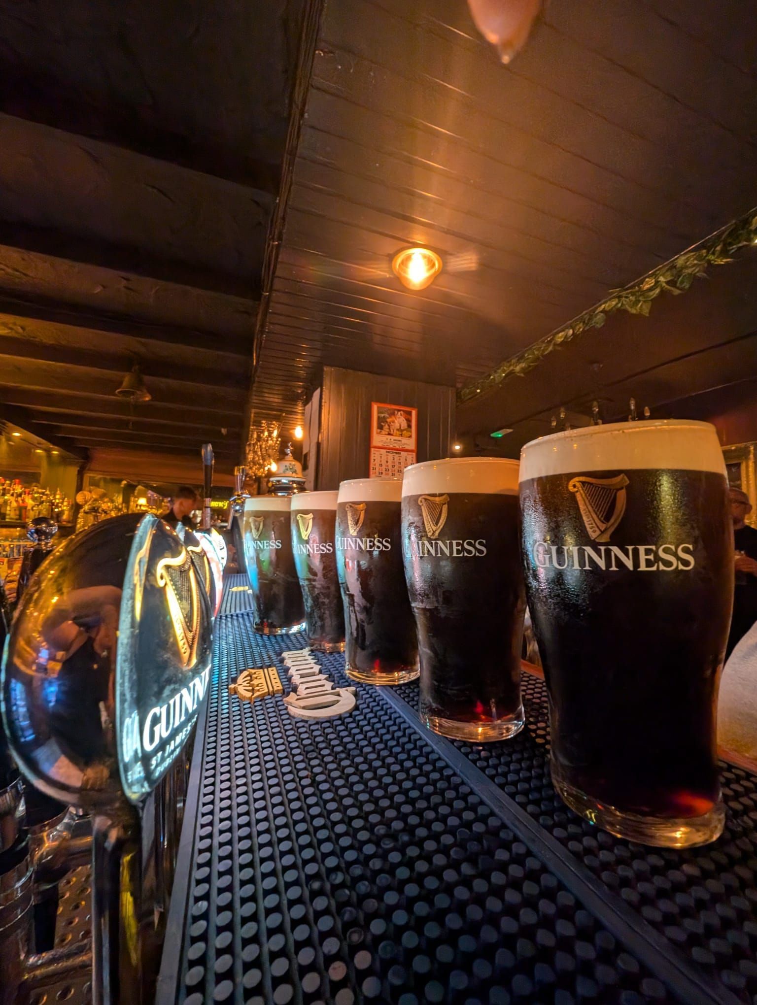 Row of Guinness pints on a bar, next to the tap. 