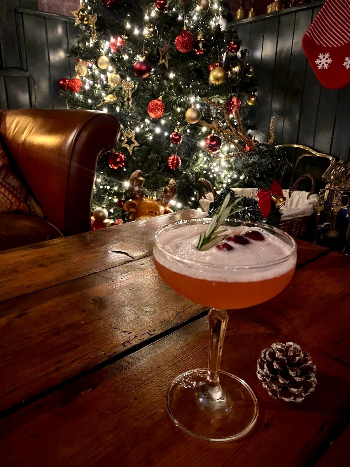 Cocktail on a wooden table, Christmas tree with lights in the background. 