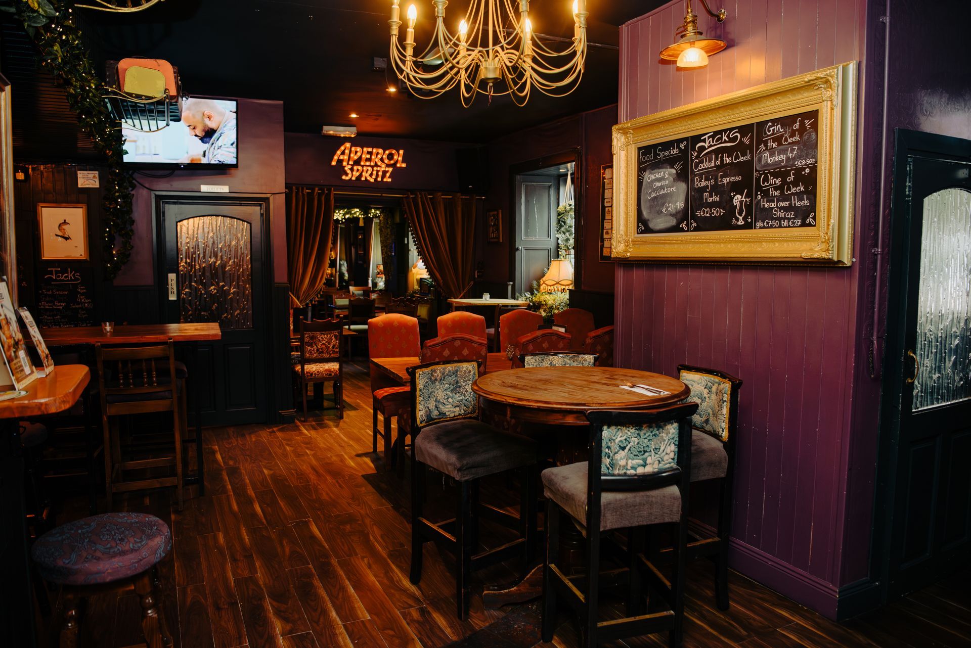 Interior of a pub with purple walls, wooden floors, and a round table with chairs.