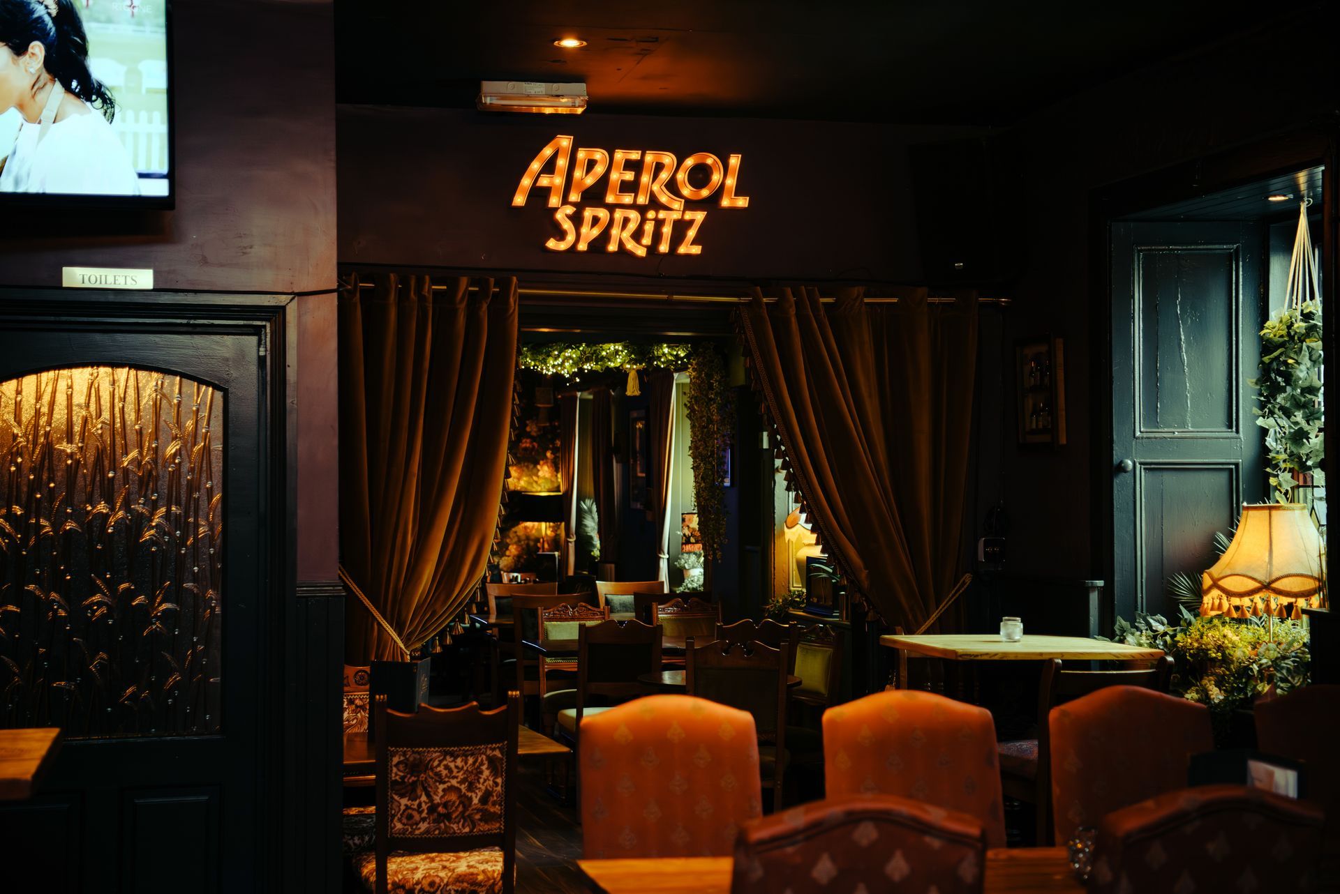 Interior of a bar, illuminated with orange light, Aperol Spritz sign above an entrance.