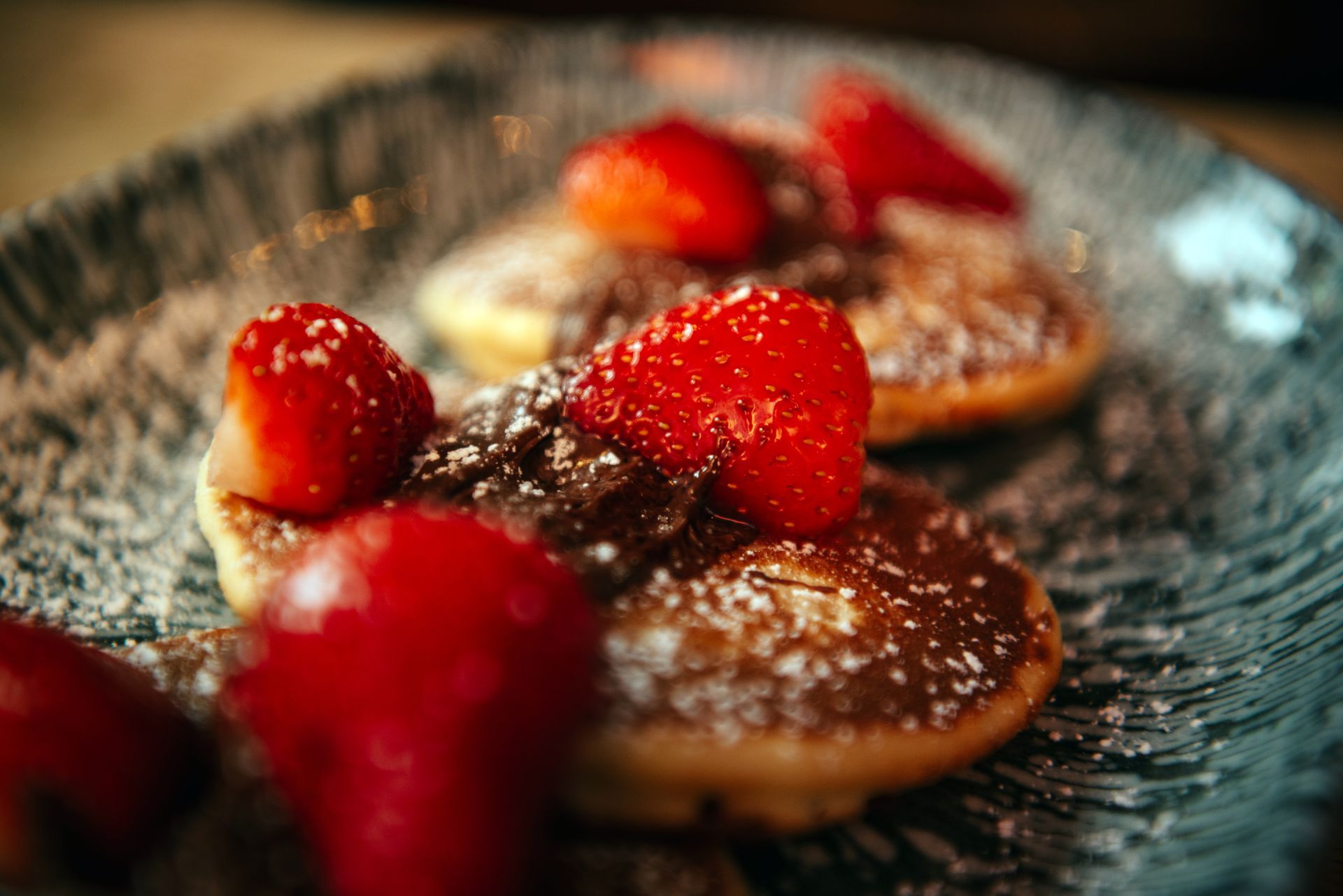 Pancakes topped with strawberries and powdered sugar on a gray plate.