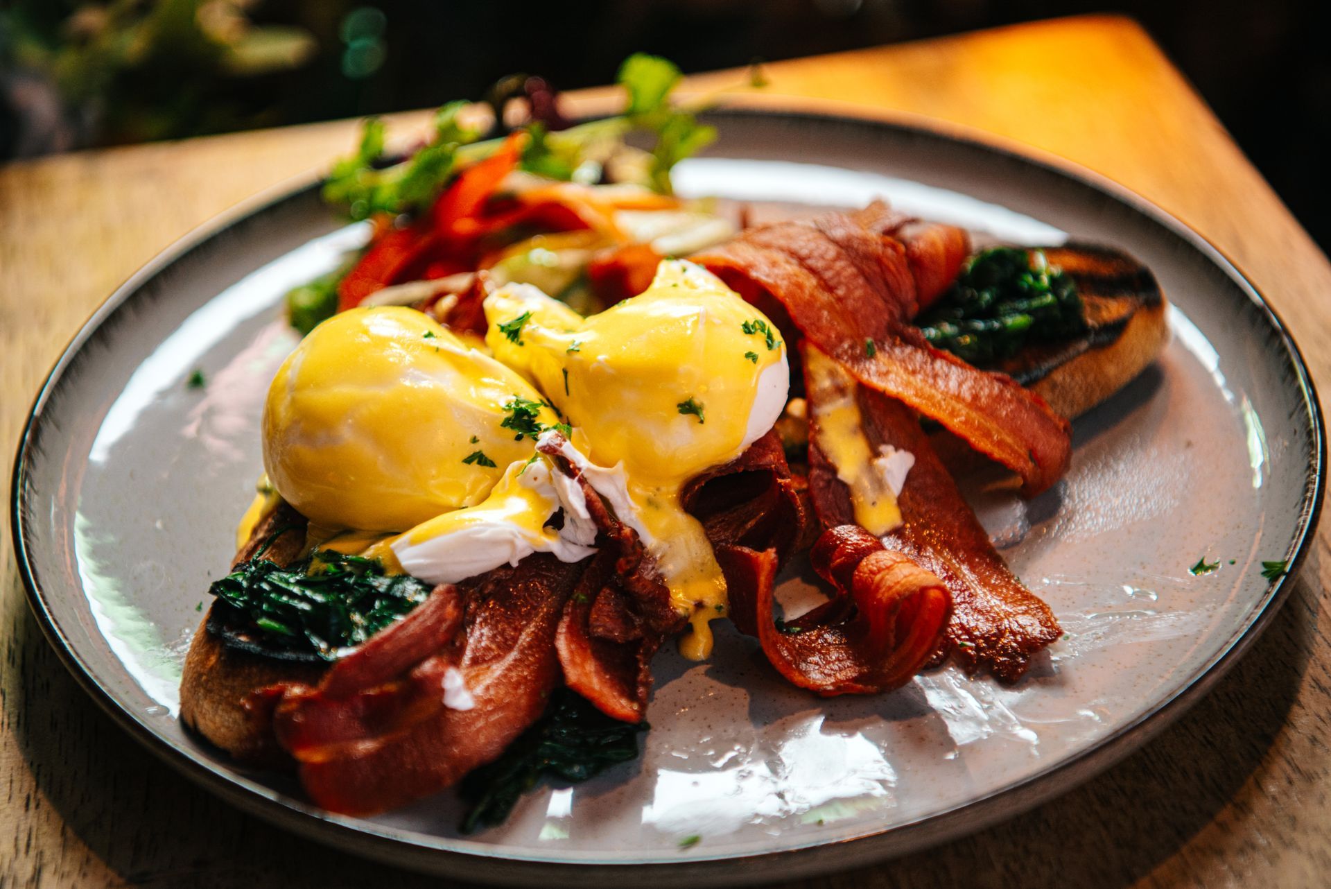Eggs Benedict with bacon and salad on a gray plate, wooden table.