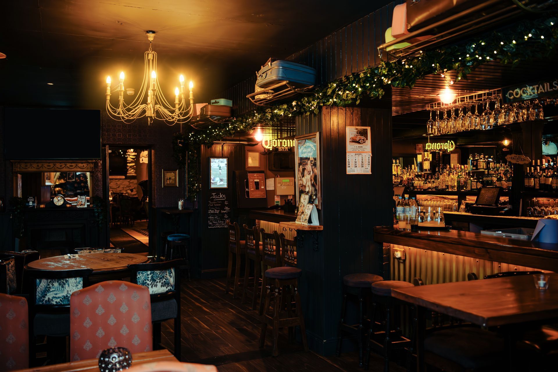 Dimly lit pub interior with a chandelier, bar, tables, and decorations.