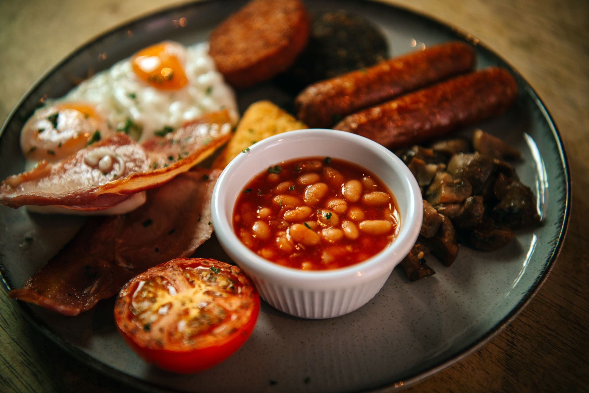 Full breakfast plate with eggs, bacon, sausage, beans, tomato, mushrooms, and hash brown.