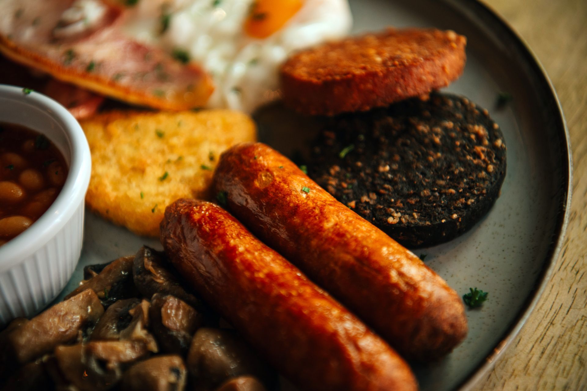 Full English breakfast on a plate: sausages, black pudding, beans, eggs, bacon, mushrooms, and a hash brown.