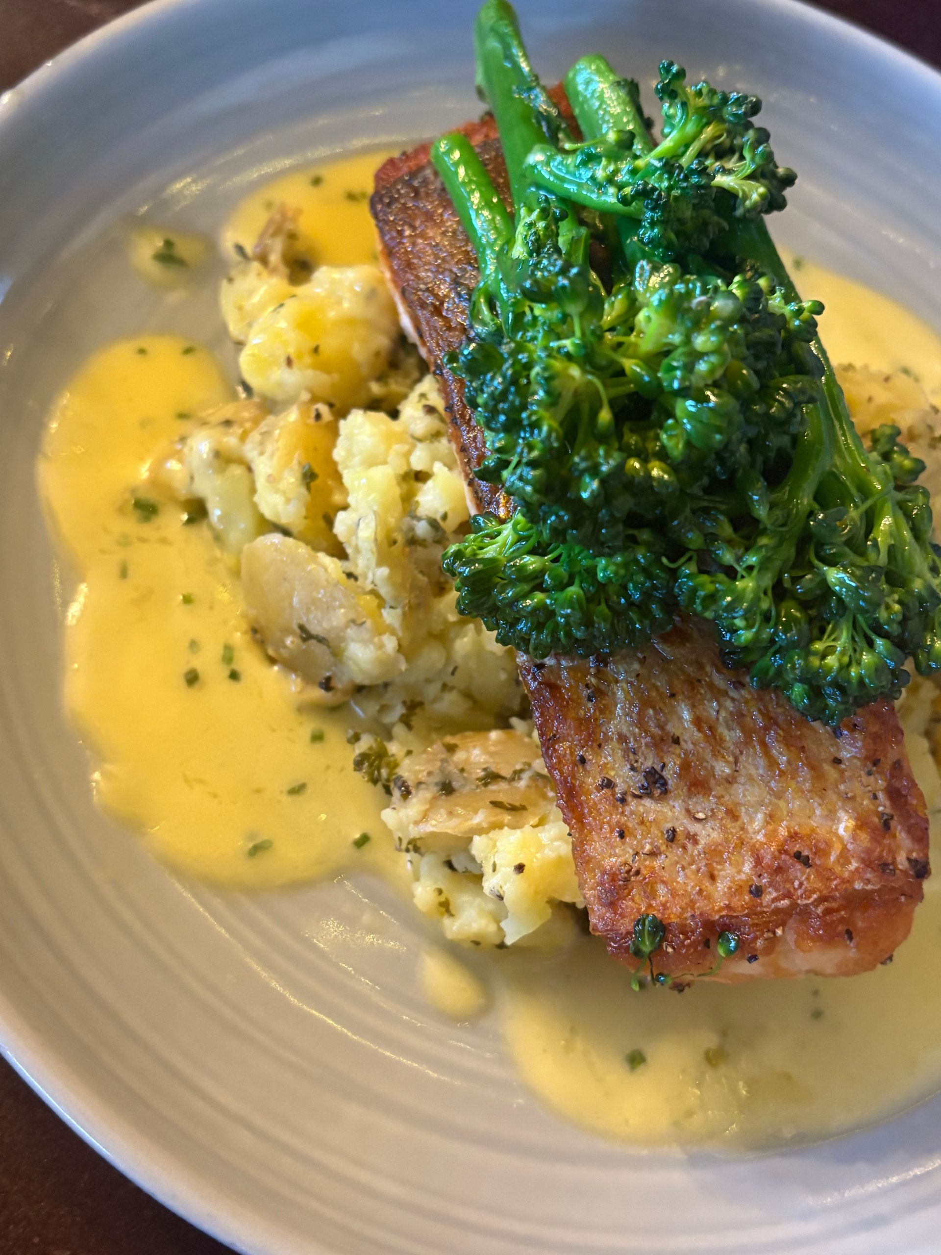 Seared salmon with broccoli, mashed potatoes, and creamy sauce on a plate.