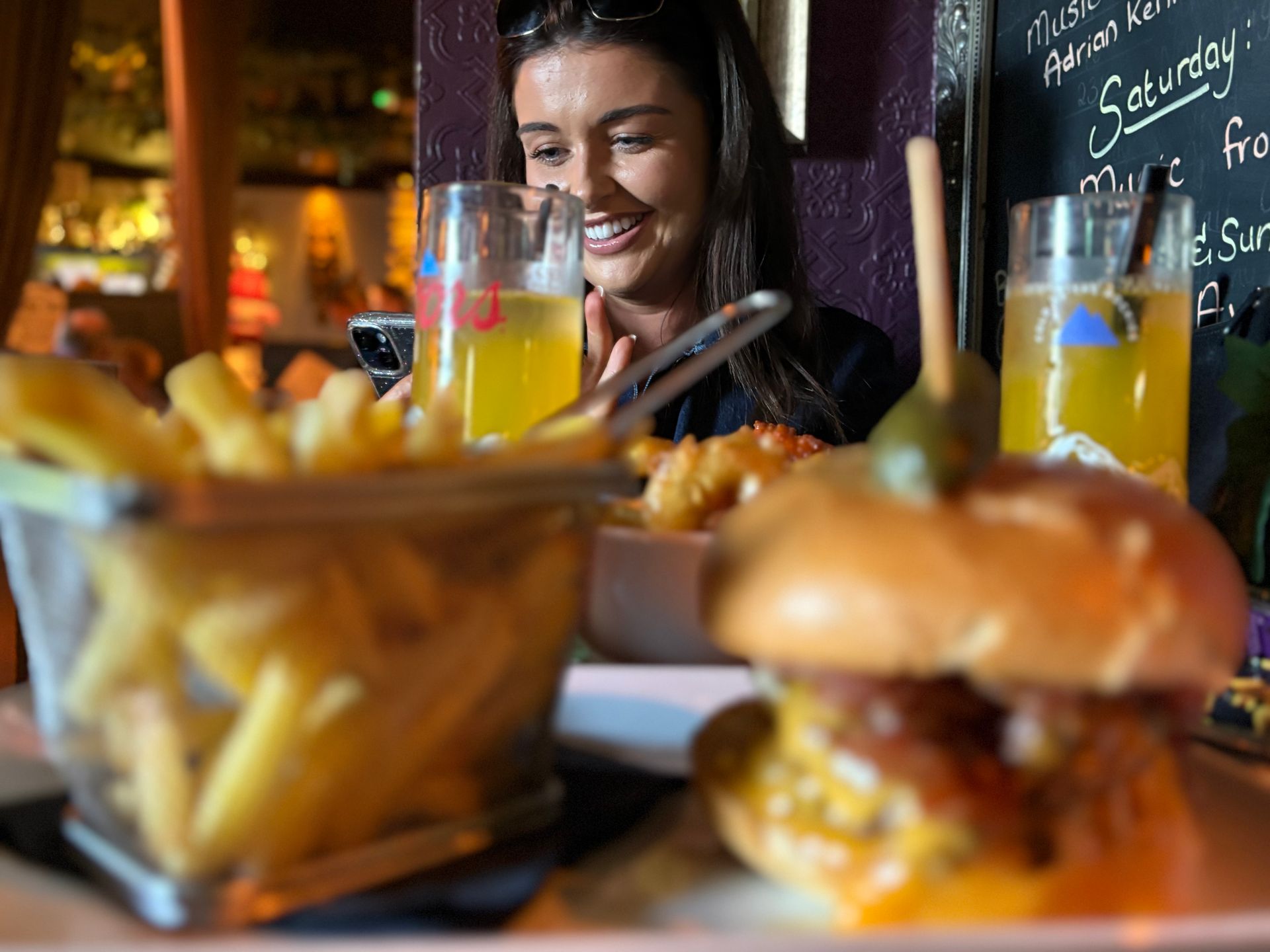 Woman smiling at a burger and fries at a restaurant table. 