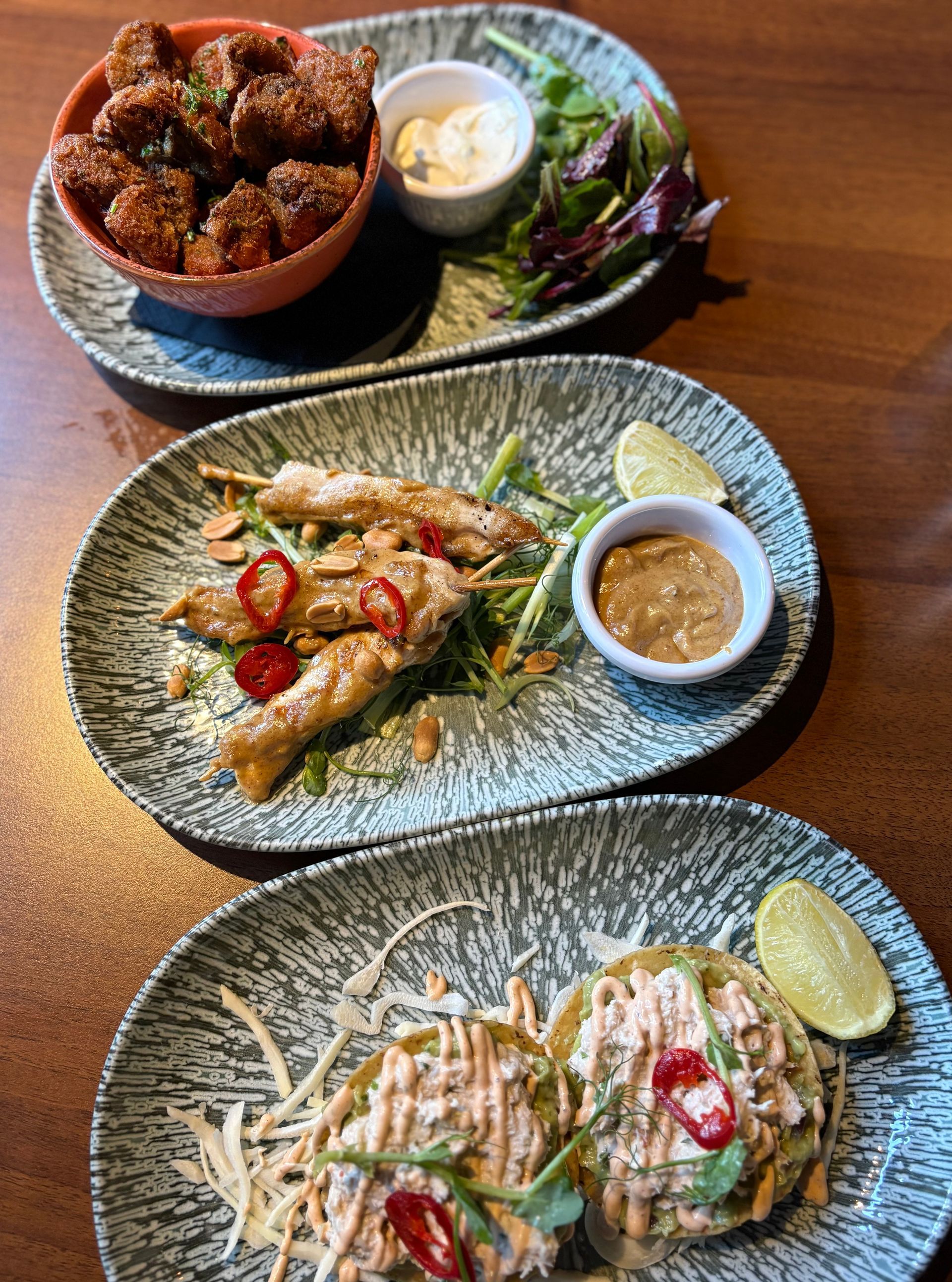 Three plates of appetizers: fried food with dipping sauces.