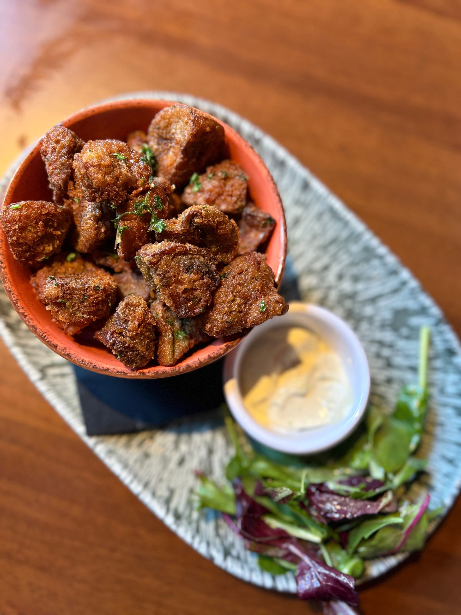 Fried mushroom appetizer in a bowl with dipping sauce and salad on a plate.