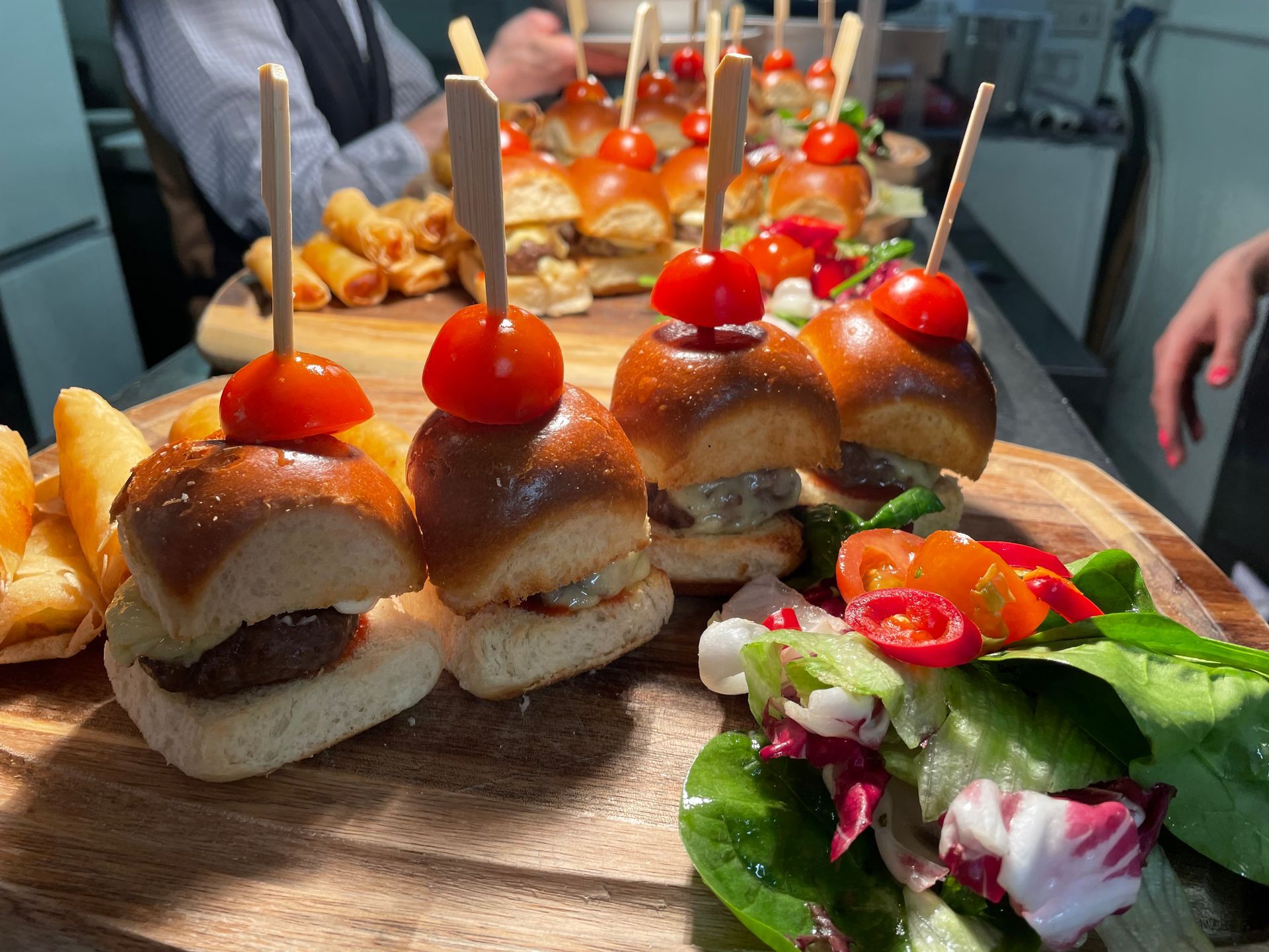 Sliders with tomato skewers and salad on a wooden board.