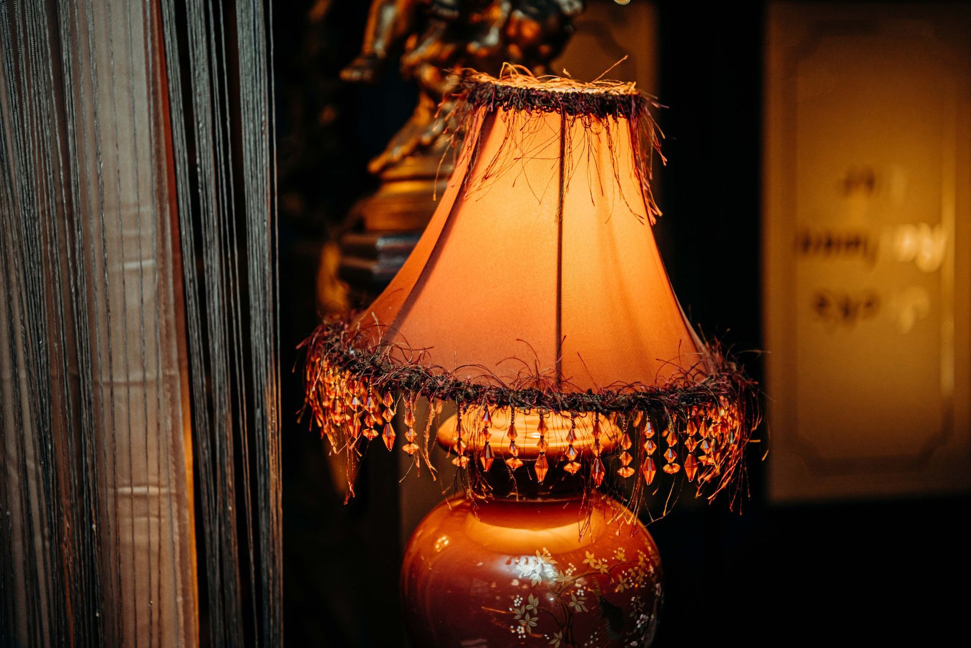 Ornate orange lampshade with beaded fringe, set against a dark background, in a dimly lit room.